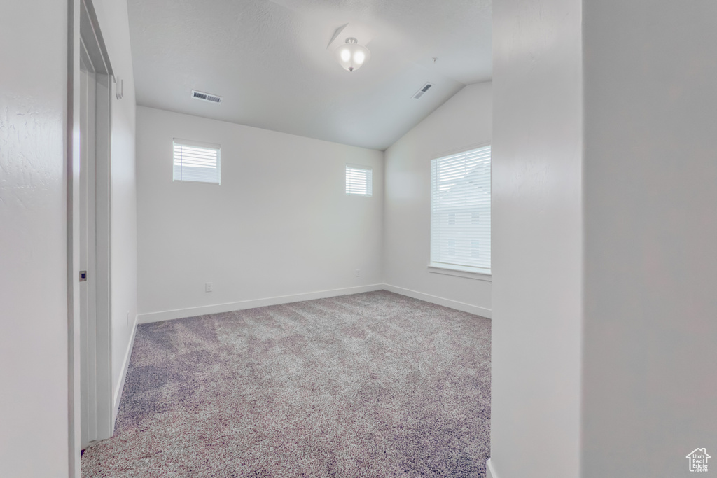 Carpeted empty room with vaulted ceiling and baseboards