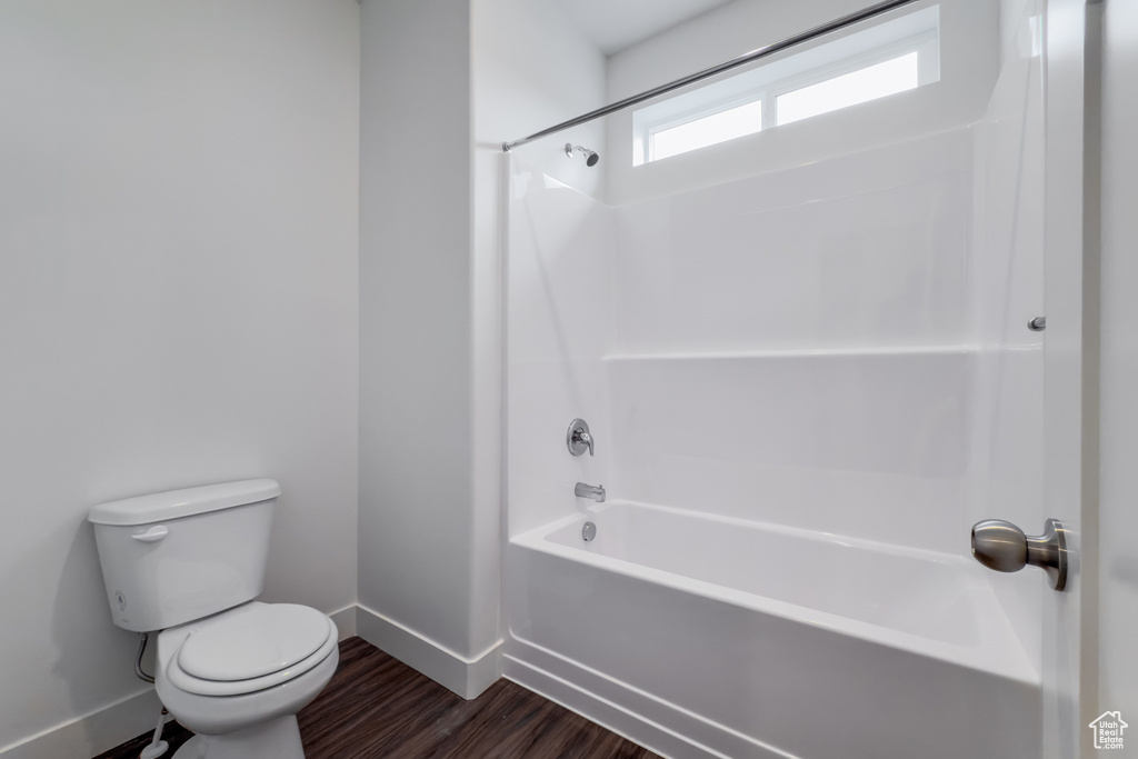 Full bathroom featuring toilet, baseboards, wood finished floors, and tub / shower combination