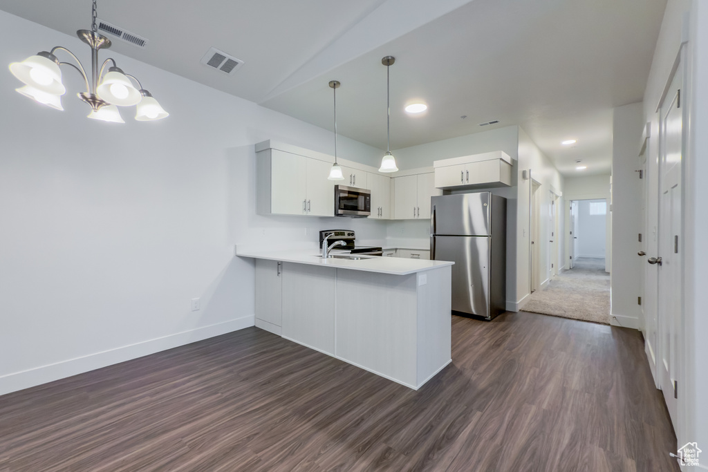 Kitchen featuring appliances with stainless steel finishes, a peninsula, light countertops, dark wood-style floors, and recessed lighting