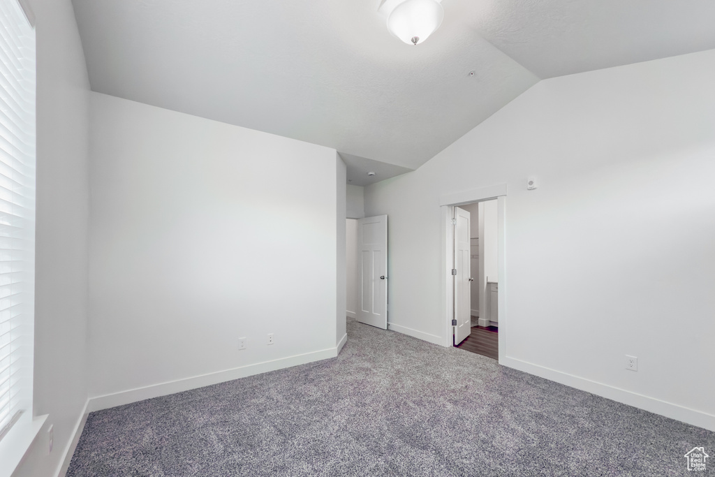 Unfurnished bedroom with lofted ceiling, carpet floors, baseboards, and ensuite bath