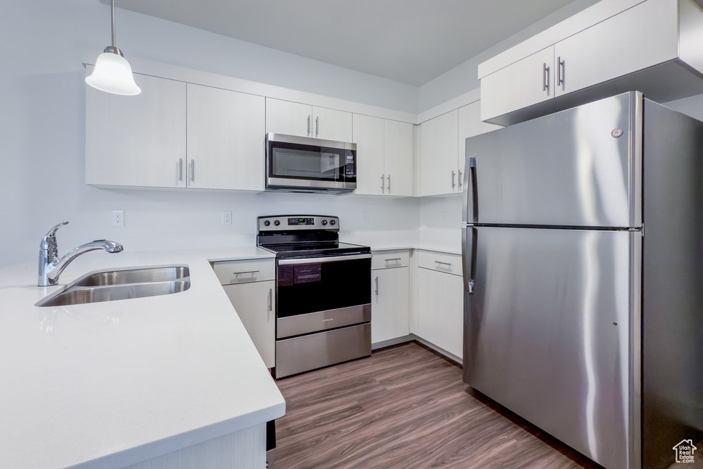 Kitchen featuring stainless steel appliances, a sink, light countertops, dark wood finished floors, and white cabinetry