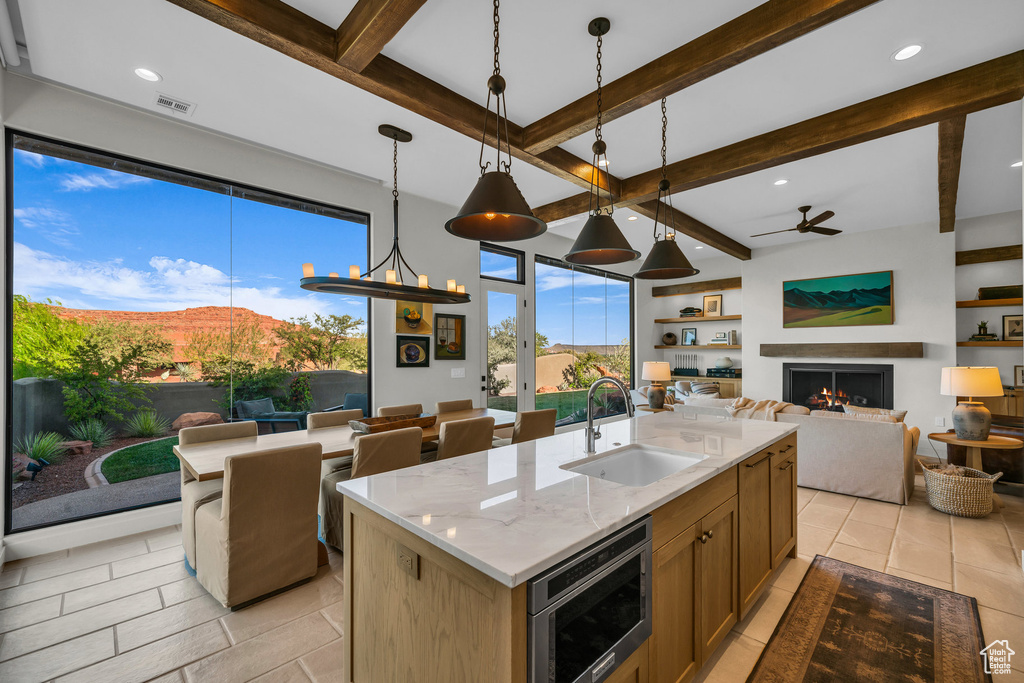 Kitchen with a sink, open floor plan, stainless steel microwave, beamed ceiling, and ceiling fan