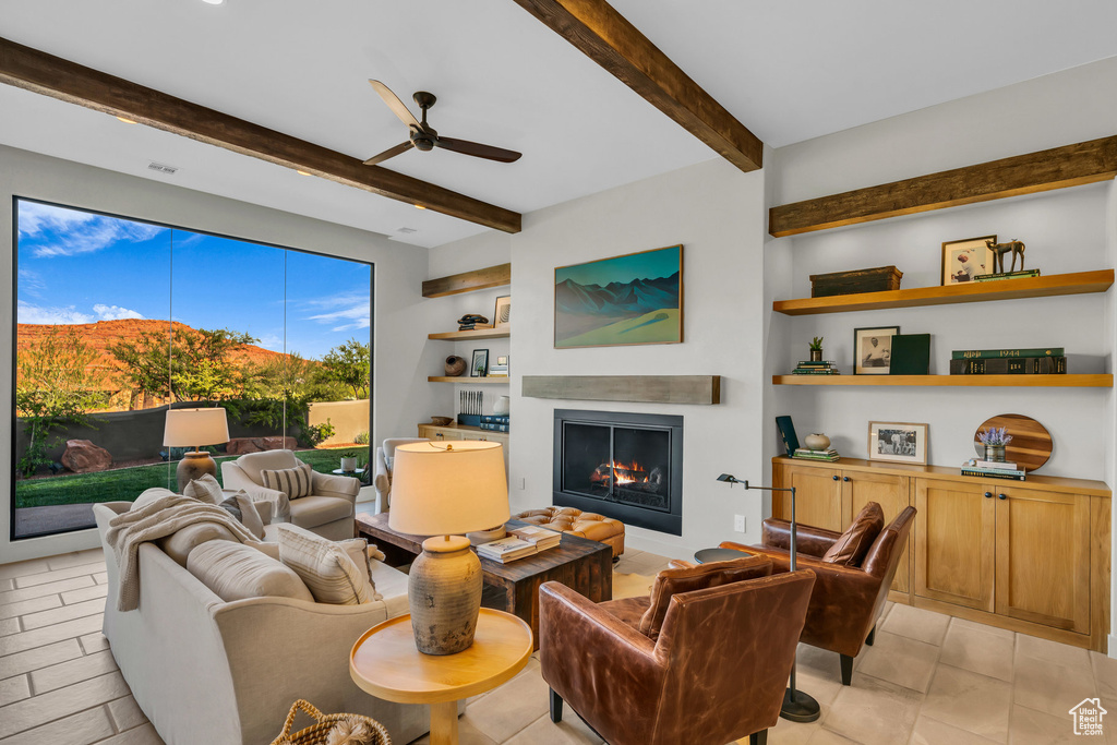 Living area with a lit fireplace, a ceiling fan, beam ceiling, and built in features