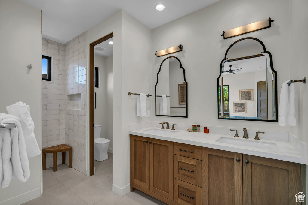 Bathroom featuring toilet, double vanity, tile patterned flooring, and tiled shower