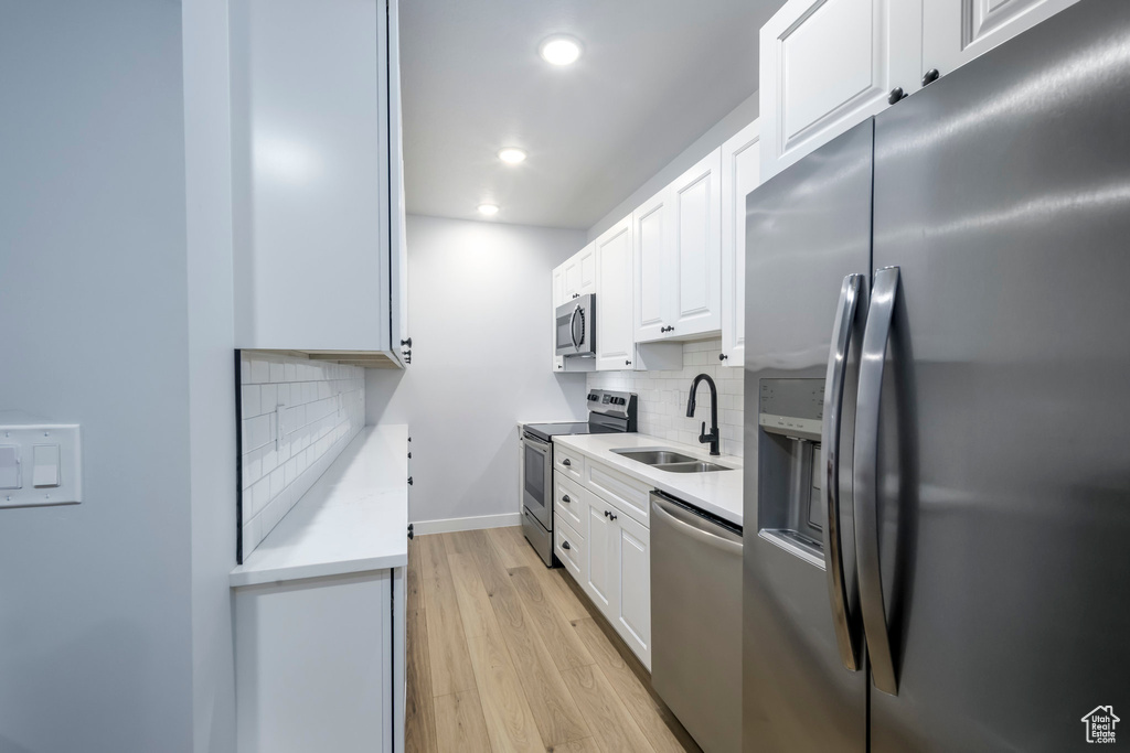 Kitchen featuring stainless steel appliances, a sink, light countertops, white cabinetry, and recessed lighting