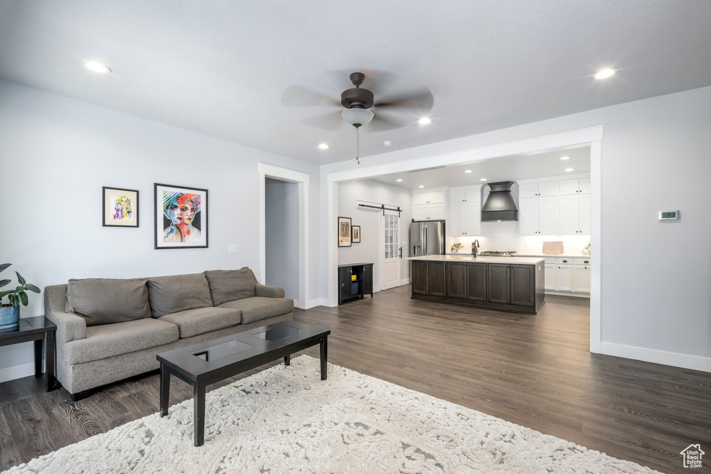 Living room featuring a barn door, ceiling fan, dark wood finished floors, recessed lighting, and baseboards