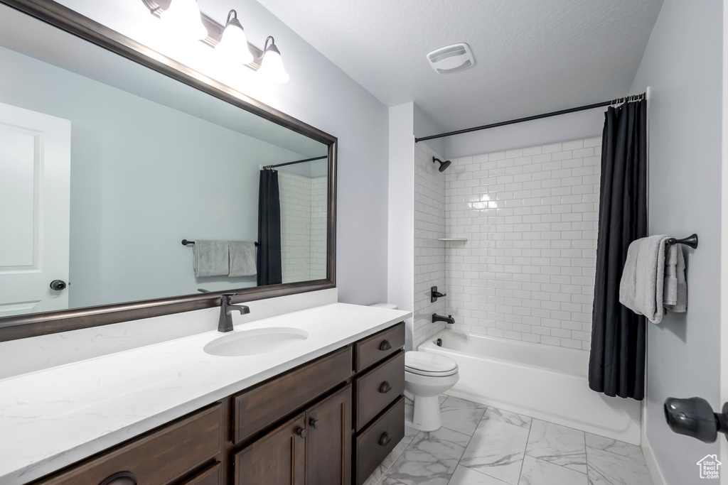 Full bathroom featuring vanity, shower / bath combo with shower curtain, toilet, and marble finish floors