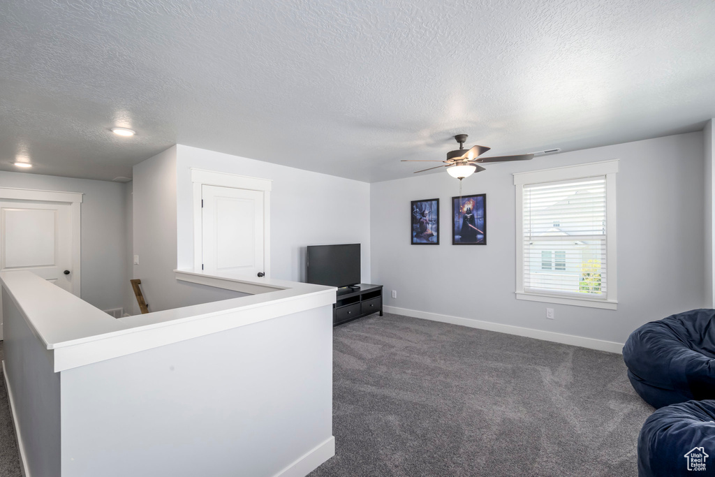 Living area featuring a textured ceiling, baseboards, dark carpet, and ceiling fan