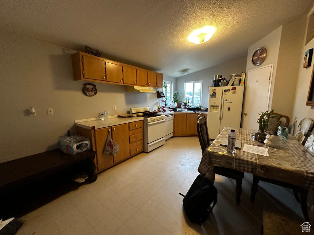 Kitchen with white appliances, vaulted ceiling, brown cabinets, under cabinet range hood, and light flooring
