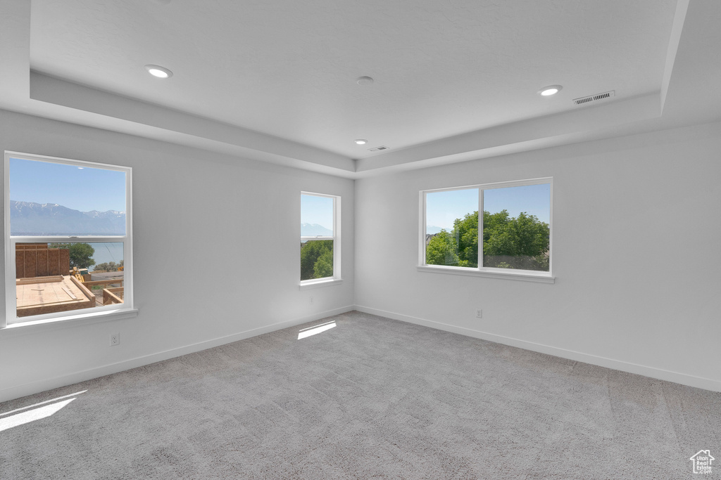 Carpeted empty room featuring a raised ceiling, baseboards, and recessed lighting