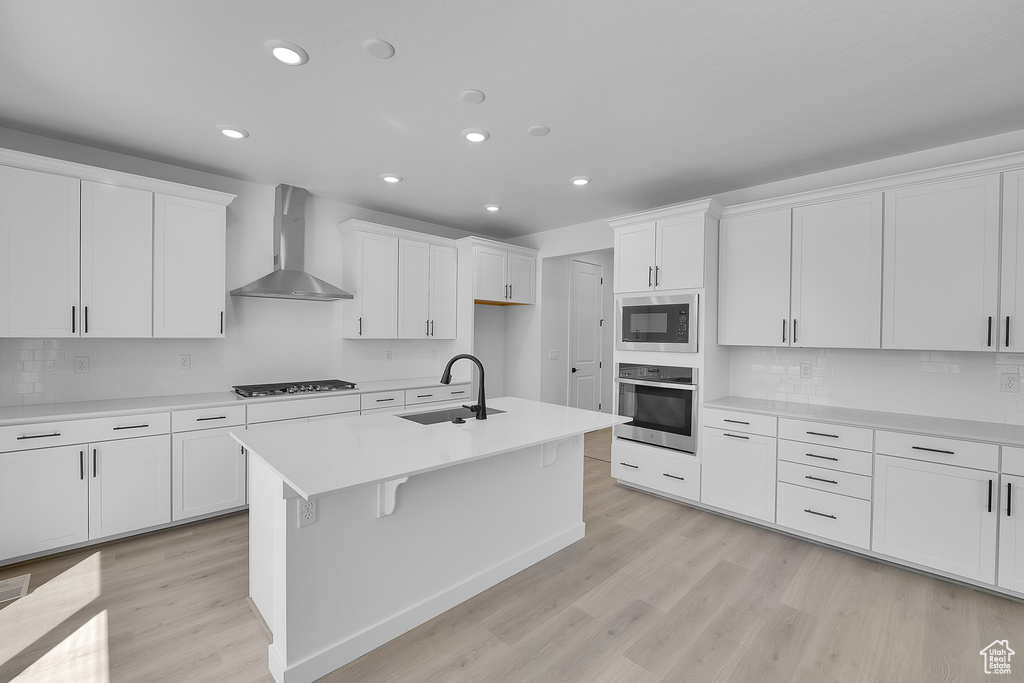 Kitchen featuring stainless steel oven, wall chimney exhaust hood, a sink, built in microwave, and light wood-type flooring