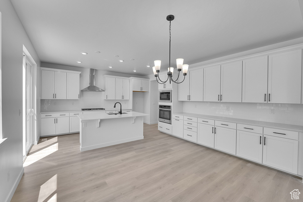 Kitchen featuring stainless steel appliances, wall chimney exhaust hood, a sink, tasteful backsplash, and white cabinets
