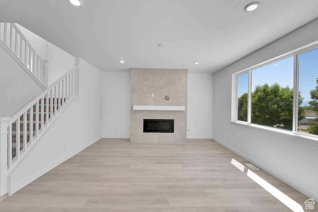 Unfurnished living room featuring stairway, recessed lighting, a tiled fireplace, baseboards, and light wood-style floors