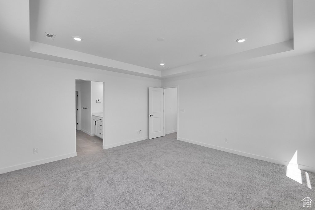 Unfurnished bedroom with a tray ceiling, baseboards, recessed lighting, carpet flooring, and ensuite bath