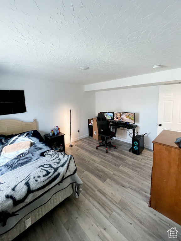 Bedroom with a textured ceiling, light wood-type flooring, an office area, and baseboards