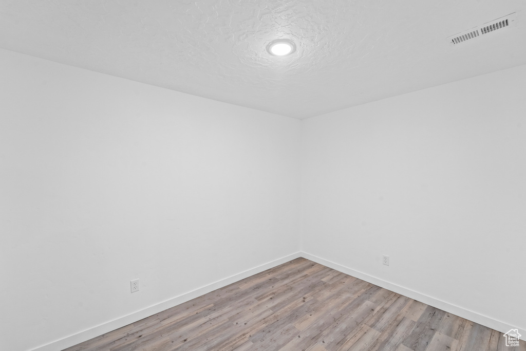 Empty room featuring light wood-style flooring, baseboards, and a textured ceiling