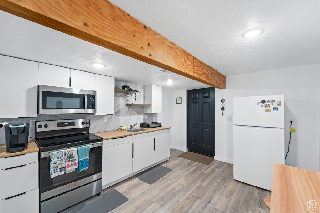 Kitchen with appliances with stainless steel finishes, a sink, white cabinetry, light countertops, and a textured ceiling