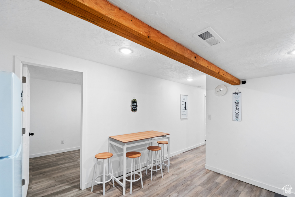 Bar with freestanding refrigerator, beamed ceiling, wood finished floors, baseboards, and a textured ceiling