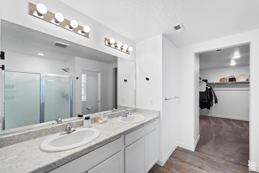 Bathroom with a shower stall, double vanity, a spacious closet, baseboards, and wood finished floors