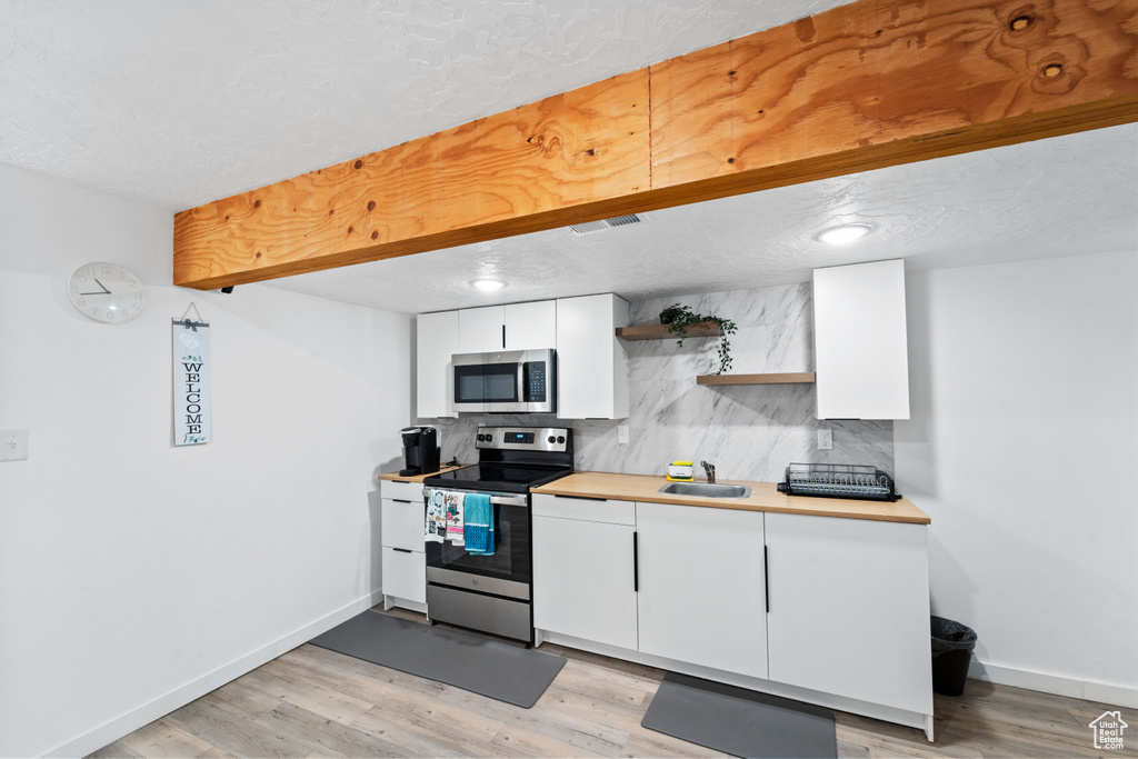 Kitchen featuring appliances with stainless steel finishes, open shelves, baseboards, white cabinets, and a textured ceiling