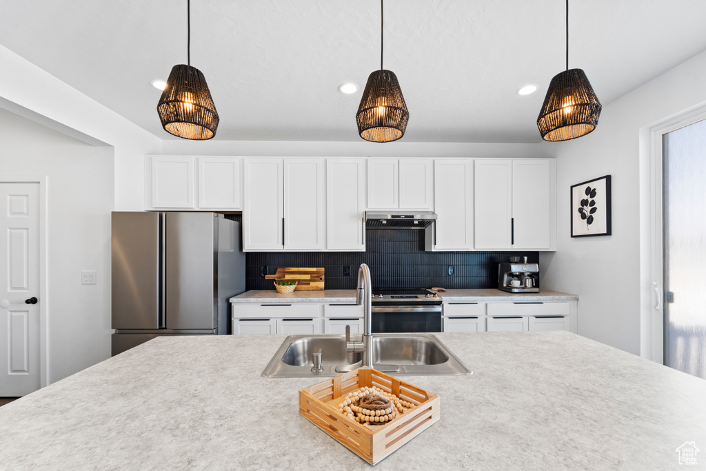 Kitchen with stainless steel appliances, under cabinet range hood, a sink, decorative light fixtures, and recessed lighting