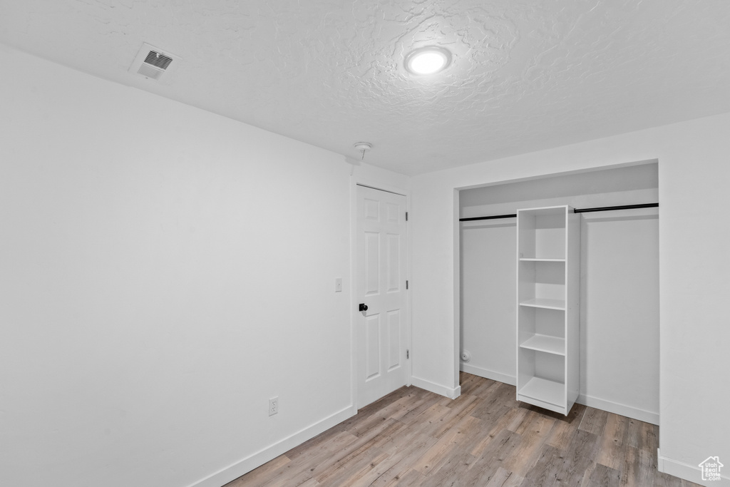 Unfurnished bedroom featuring baseboards, wood finished floors, a closet, and a textured ceiling
