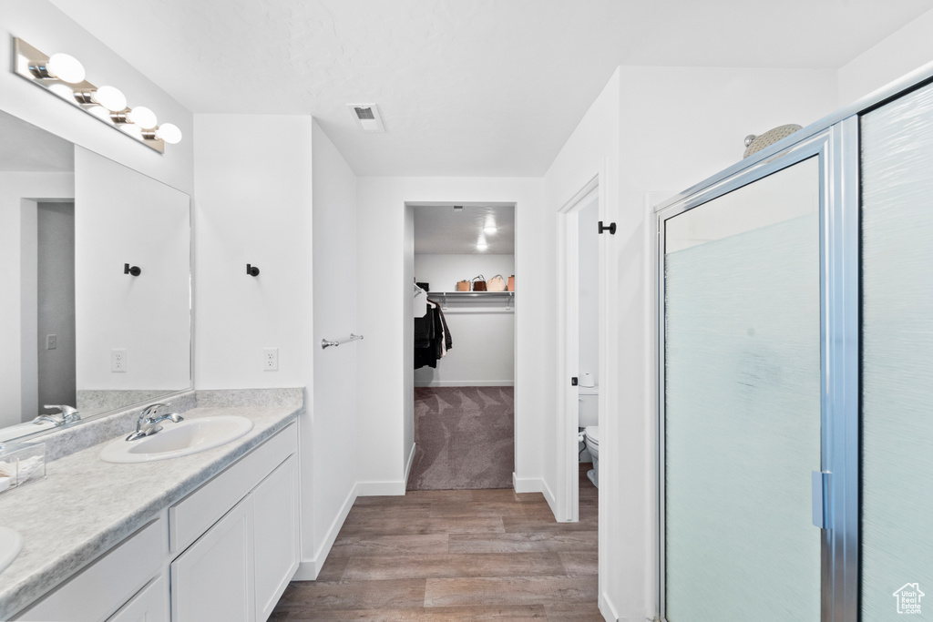 Full bath with wood finished floors, double vanity, a walk in closet, and a stall shower