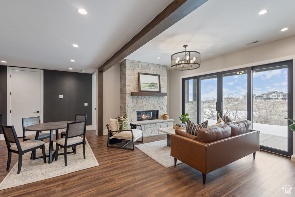 Living room featuring dark wood-style flooring, a stone fireplace, recessed lighting, a chandelier, and baseboards