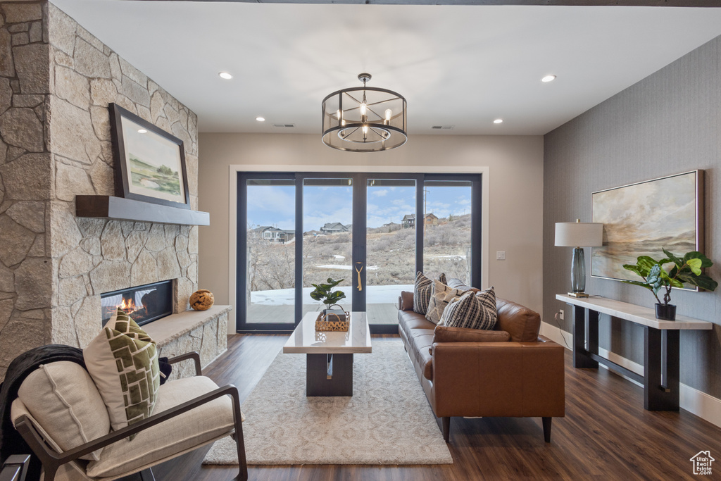 Living area featuring dark wood finished floors, a chandelier, a stone fireplace, recessed lighting, and baseboards