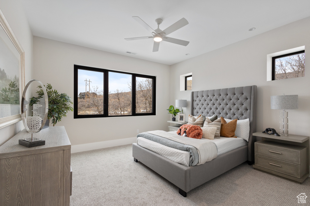 Bedroom with light colored carpet, multiple windows, baseboards, and ceiling fan