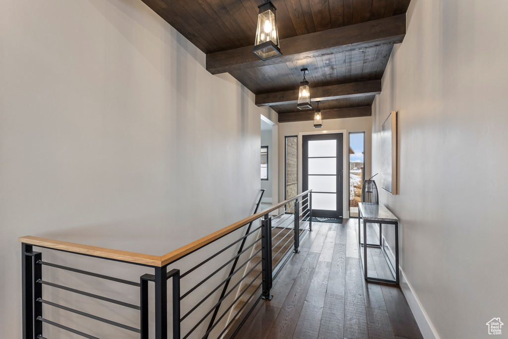 Corridor featuring an upstairs landing, wooden ceiling with exposed beams, dark wood-type flooring, and baseboards