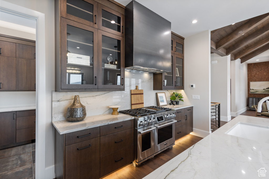 Kitchen with double oven range, a sink, wall chimney exhaust hood, dark brown cabinets, and light stone countertops