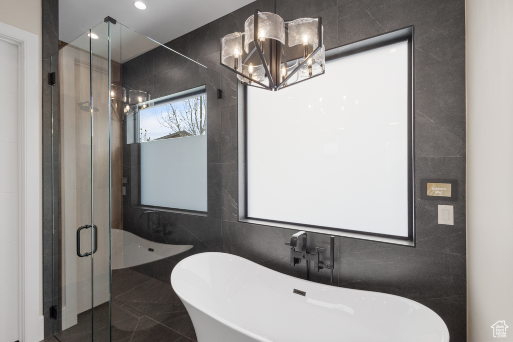 Full bath featuring tile walls, a freestanding bath, a stall shower, a chandelier, and a sink