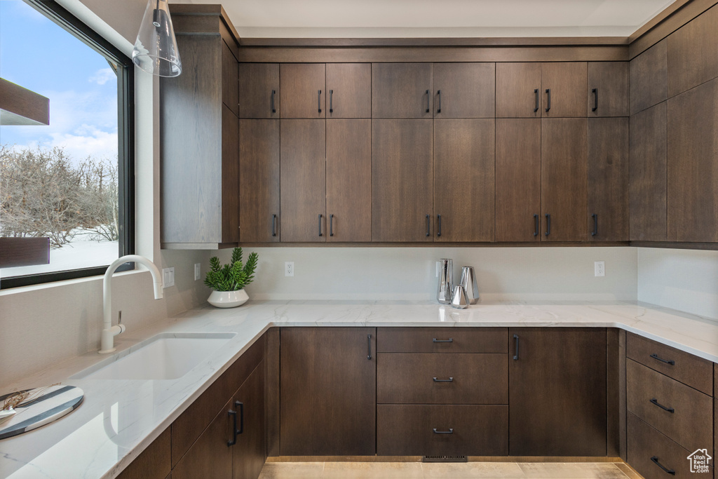 Kitchen featuring a sink, light stone counters, and dark brown cabinets