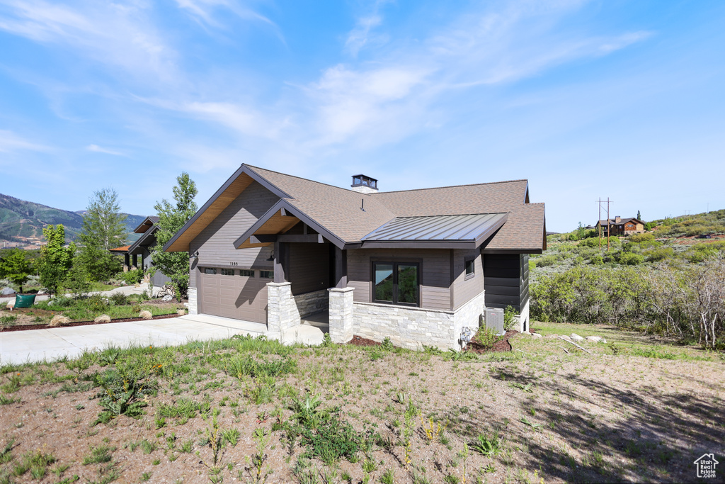 View of front of house with a standing seam roof, stone siding, driveway, metal roof, and a garage