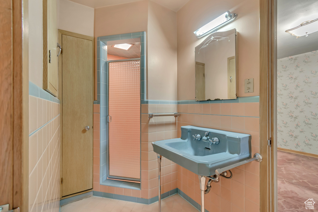 Bathroom with wainscoting, wallpapered walls, tile walls, and a sink