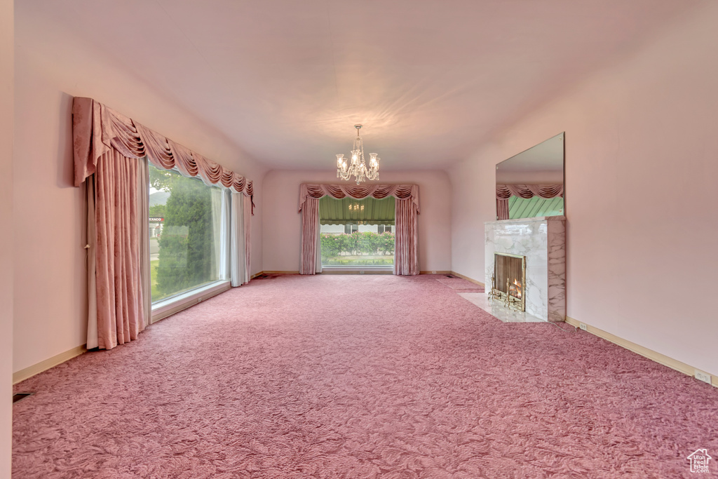 Unfurnished living room with a chandelier, carpet flooring, a fireplace, and baseboards