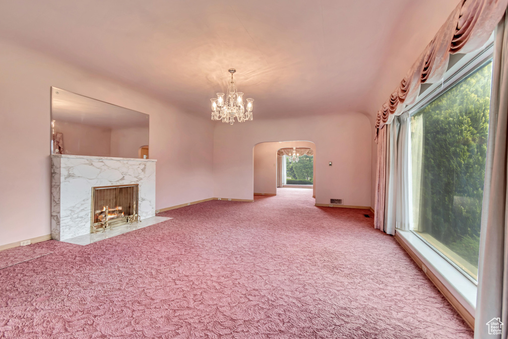 Unfurnished living room featuring arched walkways, carpet floors, a chandelier, a high end fireplace, and baseboards