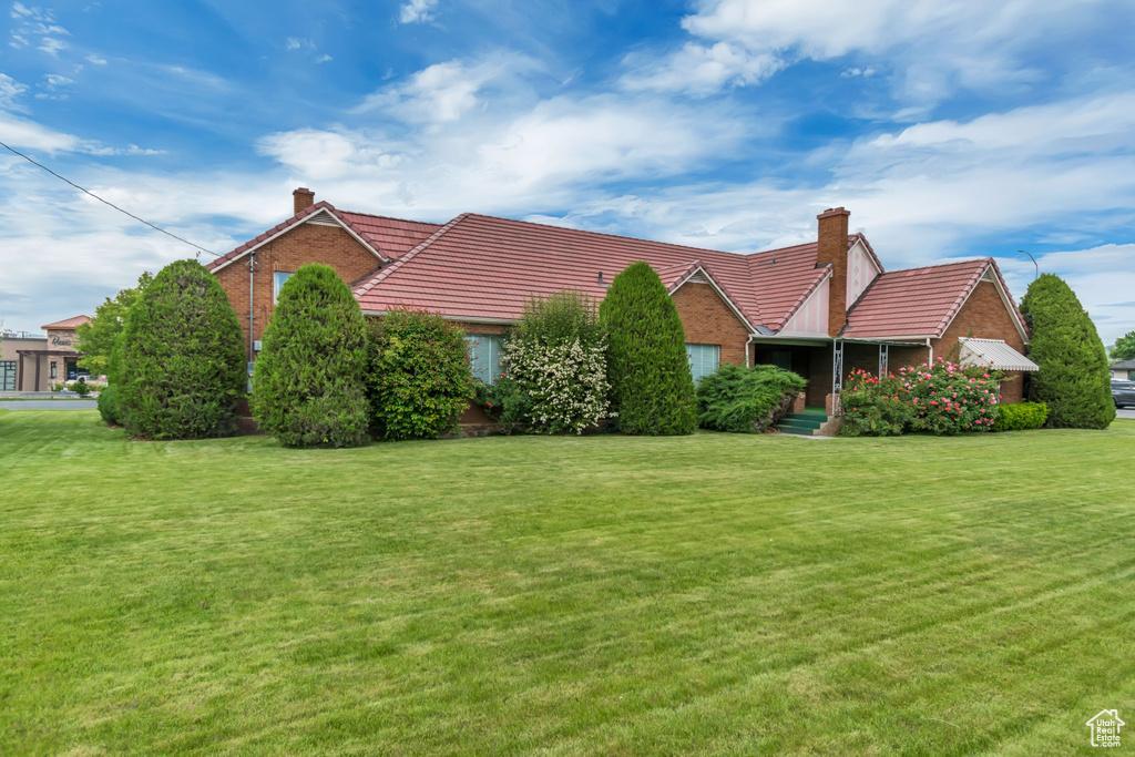 View of front of house featuring a chimney, a tiled roof, a front lawn, and brick siding