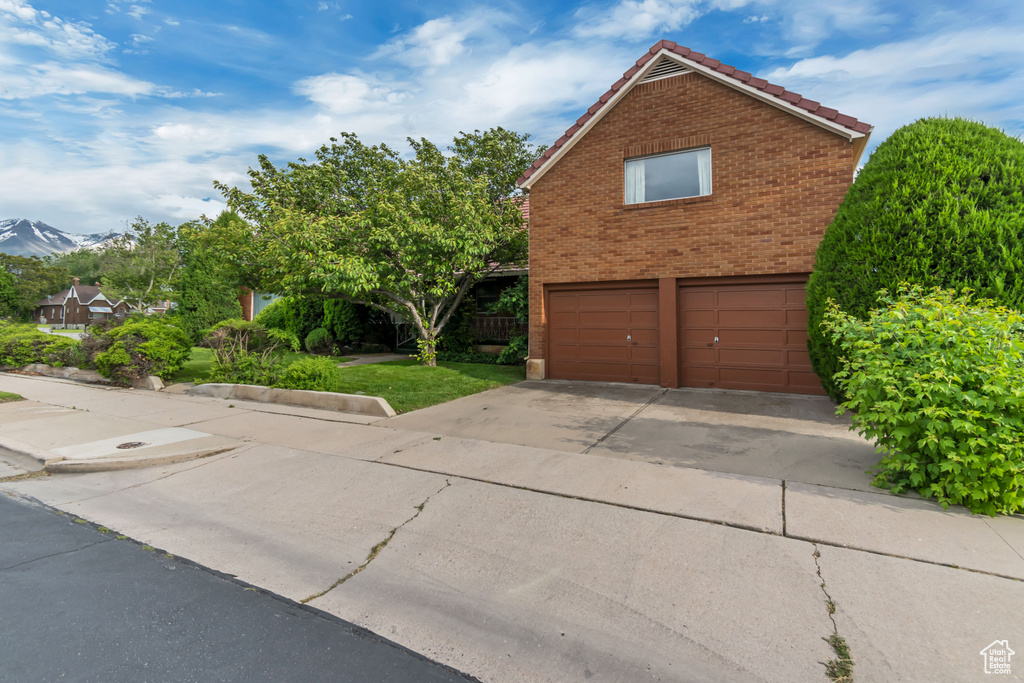 View of side of home featuring an attached garage, a tiled roof, brick siding, concrete driveway, and a mountain view