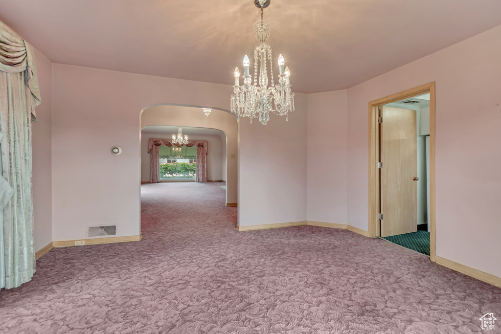 Carpeted spare room featuring arched walkways, a chandelier, and baseboards