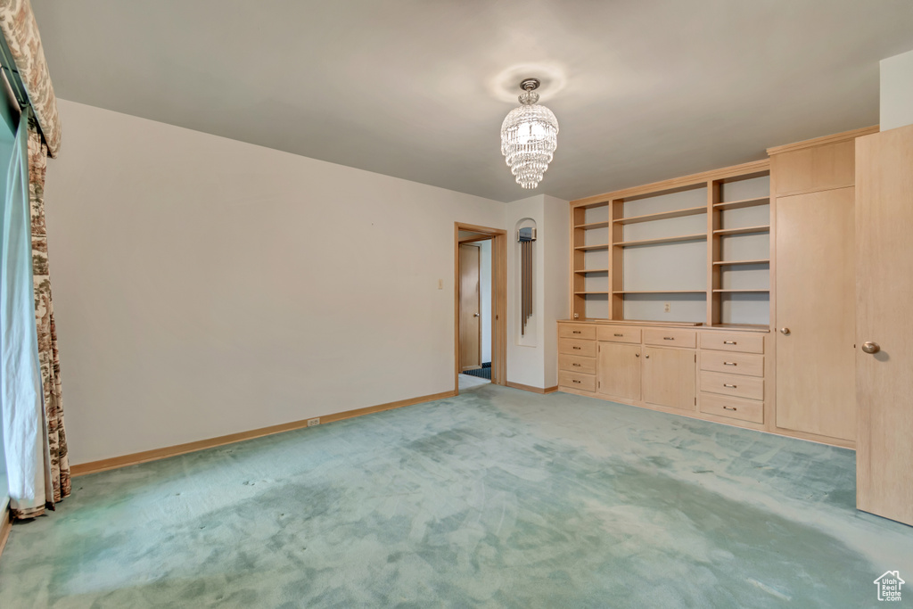 Unfurnished bedroom featuring a chandelier, light carpet, and baseboards