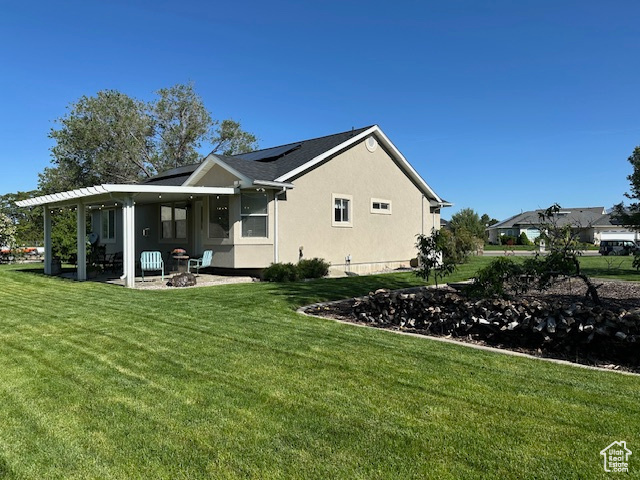 Back of house with a patio, roof mounted solar panels, a yard, and stucco siding