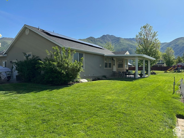 View of side of property with a mountain view, a patio area, roof mounted solar panels, and a yard