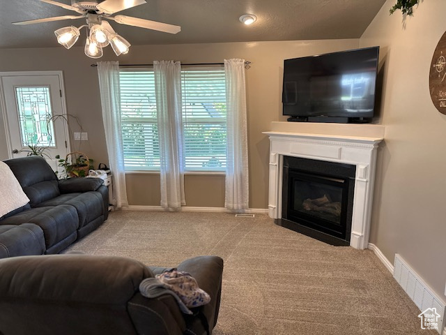Living area with ceiling fan, carpet flooring, a glass covered fireplace, and baseboards