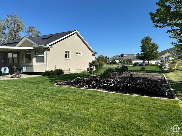 View of property exterior featuring a lawn, solar panels, stucco siding, and an outdoor fire pit