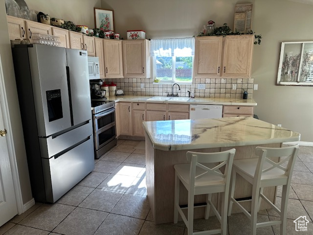 Kitchen featuring stainless steel appliances, a sink, light brown cabinetry, decorative backsplash, and light tile patterned flooring