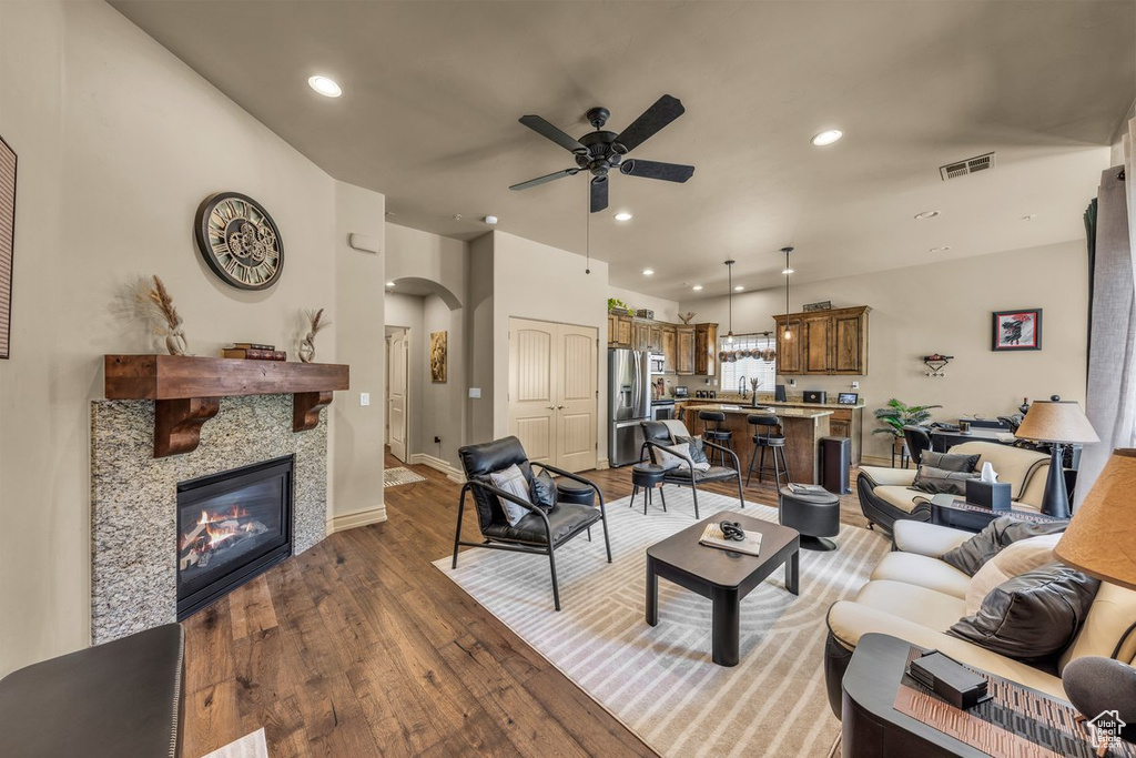 Living room with ceiling fan, arched walkways, dark wood-type flooring, recessed lighting, and a tiled fireplace