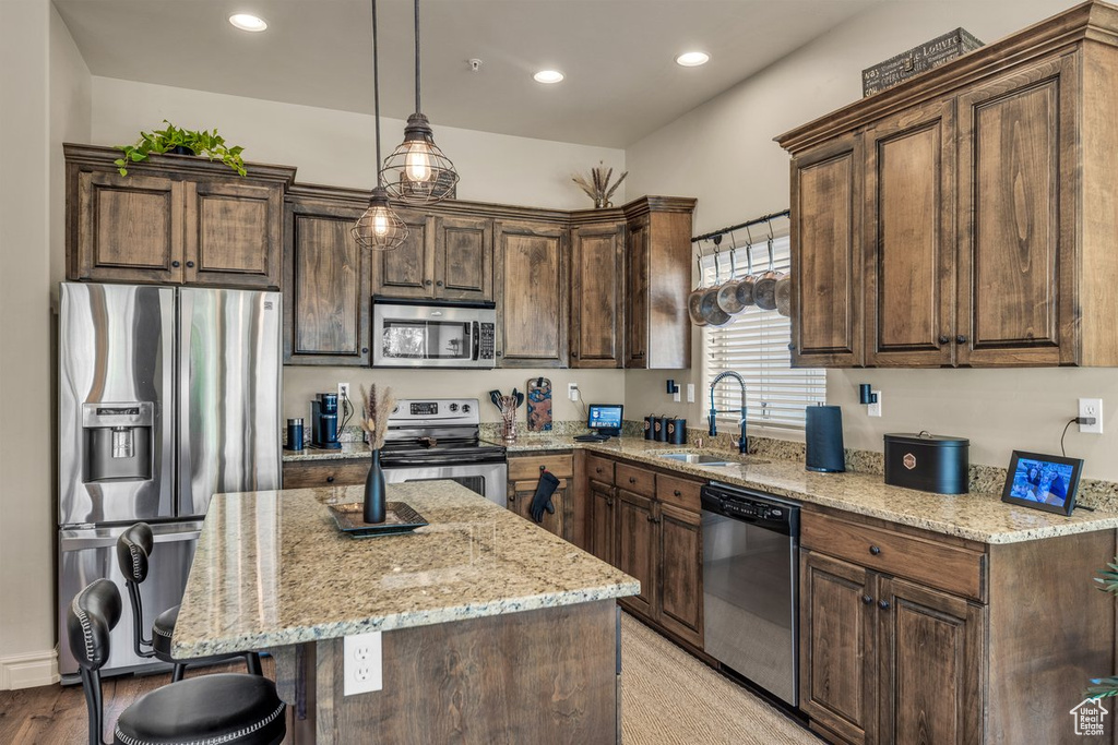 Kitchen featuring stainless steel appliances, a sink, a kitchen bar, light stone counters, and recessed lighting