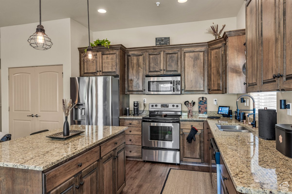 Kitchen with appliances with stainless steel finishes, a sink, light stone counters, dark wood finished floors, and a center island